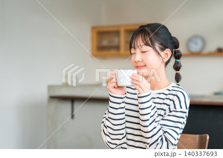 自宅のリビングでホットドリンクを飲む小学生,中学生の女の子 140337693