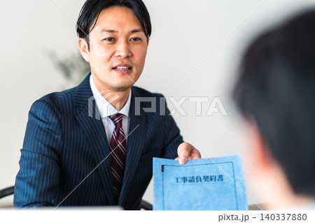 工事請負契約書を提示して笑顔で説明するスーツ姿の男性ビジネスマン 工事請負契約書を提示して笑顔で説明するスーツ姿の男性ビジネスマン 140337880