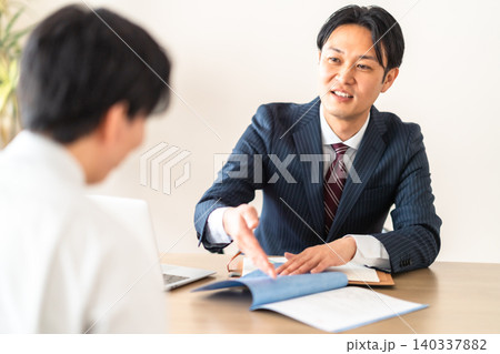 工事請負契約書を提示して笑顔で説明するスーツ姿の男性ビジネスマン 140337882