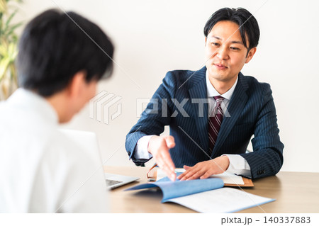 工事請負契約書を提示して笑顔で説明するスーツ姿の男性ビジネスマン 140337883