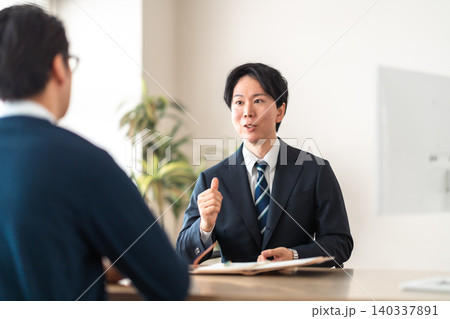 商談や打合せで身を乗り出して熱心に話すスーツ姿の男性 商談や打合せで身を乗り出して熱心に話すスーツ姿の男性 140337891