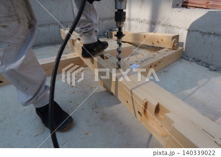 Japanese carpenter drilling holes in wooden foundation beam at construction site Japanese carpenter drilling holes in wooden foundation beam at construction site 140339022