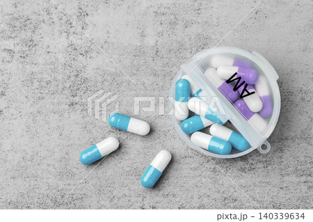 Pills spilling with open daily pill organizer on a grey concrete background, top view Pills spilling with open daily pill organizer on a grey concrete background, top view 140339634