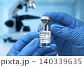 A researcher in blue gloves holds a vial labeled Ebola vaccine 140339635