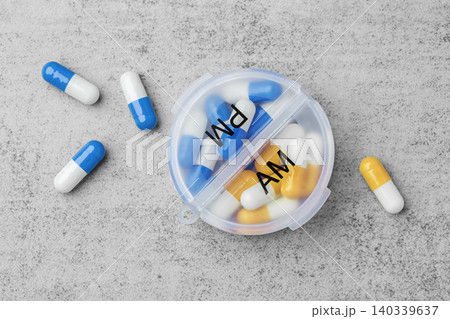 Daily pill box organizer with AM and PM compartments with blue and yellow capsules on a grey concrete background Daily pill box organizer with AM and PM compartments with blue and yellow capsules on a grey concrete background 140339637