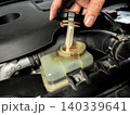 A mechanic opens the power steering fluid reservoir cap with an attached dipstick 140339641