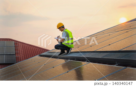 Worker inspects solar panels on a sloped roof Worker inspects solar panels on a sloped roof 140340147