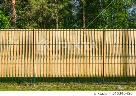 Wooden privacy slats integrated into green welded mesh fence along forest property boundary line 140340450