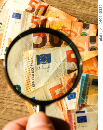 Magnifying glass checking euro banknote security features for fraud detection and authentication 140340520
