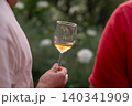 Hand holding a glass of white wine outdoors at a garden gathering in Sicily 140341909