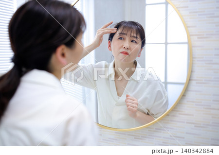 鏡を見て生え際が気になるシニアの女性 鏡を見て生え際が気になるシニアの女性 140342884