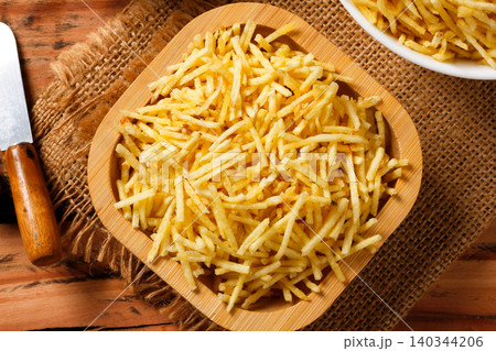 Portion of golden shoestring potatoes served on a rustic wooden serving platter, accompanied by an antique knife and burlap cloth Portion of golden shoestring potatoes served on a rustic wooden serving platter, accompanied by an antique knife and burlap cloth 140344206