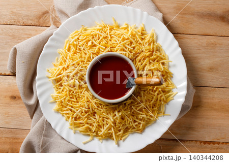 A portion of golden shoestring potatoes served on a white ceramic plate with a ketchup bottle in the center A portion of golden shoestring potatoes served on a white ceramic plate with a ketchup bottle in the center 140344208