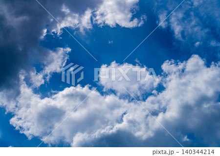 A view of white clouds against a blue sky, with the light from the sun shining through between fluffy mass 140344214