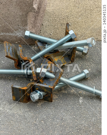 Close-up of steel bolts and rusty brackets on asphalt - industrial construction hardware, engineering, repair and maintenance concept Close-up of steel bolts and rusty brackets on asphalt - industrial construction hardware, engineering, repair and maintenance concept 140345135