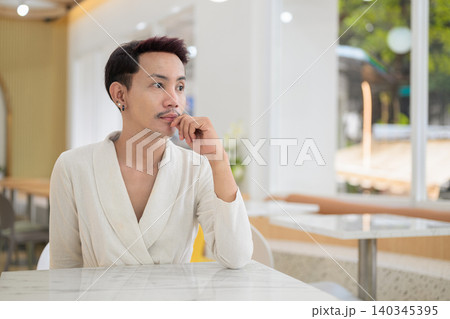 Thoughtful non-binary gay Thai man looking away while sitting at a cafe table Thoughtful non-binary gay Thai man looking away while sitting at a cafe table 140345395