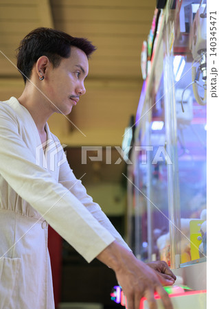 Vertical close up portrait of focused non-binary gay Thai man playing arcade claw game 140345471