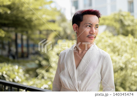 Horizontal portrait of non-binary gay Thai man looking away thoughtfully outdoors on balcony Horizontal portrait of non-binary gay Thai man looking away thoughtfully outdoors on balcony 140345474