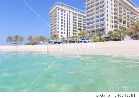 Luxurious beachfront resort setting on a sunny day with pristine waters and palm trees in clear view Luxurious beachfront resort setting on a sunny day with pristine waters and palm trees in clear view 140345591