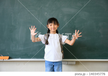 教室の黒板の前でランドセルを背負い両手を広げて笑顔を見せる小学1年生の女の子 教室の黒板の前でランドセルを背負い両手を広げて笑顔を見せる小学1年生の女の子 140345776