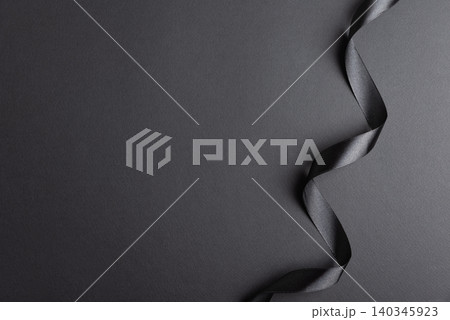 Black satin ribbon forming wavy border on dark background Black satin ribbon forming wavy border on dark background 140345923