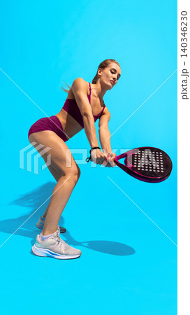 Female padel player in ready stance with racket on blue studio background. Female padel player in ready stance with racket on blue studio background. 140346230