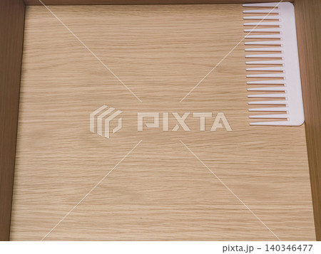 White plastic comb resting on wooden drawer surface White plastic comb resting on wooden drawer surface 140346477