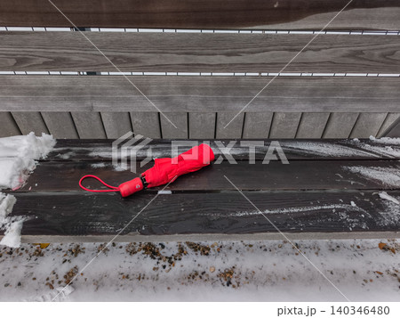 Red umbrella abandoned on a park bench in winter 140346480