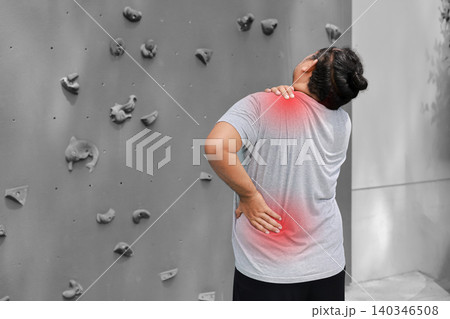 Back view of an overweight Asian man suffering from lower back and shoulder pain with glowing red graphic overlay near a rock climbing wall. Sports injury and healthcare concept. Back view of an overweight Asian man suffering from lower back and shoulder pain with glowing red graphic overlay near a rock climbing wall. Sports injury and healthcare concept. 140346508