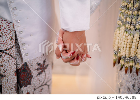 The bride and groom hold hands in a traditional Indonesian wedding ceremony. 140346589