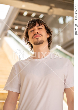 Young 25 year old man stands against a modern staircase and urban infrastructure. 140347548