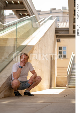 55 year old man sitting near a modern staircase and looking thoughtfully to the side. 55 year old man sitting near a modern staircase and looking thoughtfully to the side. 140347662