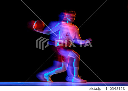 Basketball player running with ball through neon blur on black background. 140348128