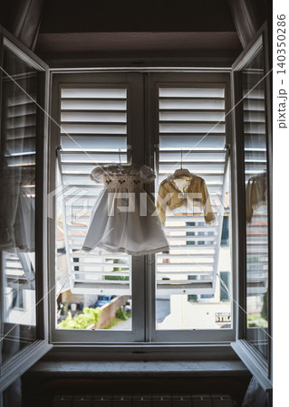 Children's Clothing Hanging by Window with Shutters Children's Clothing Hanging by Window with Shutters 140350286