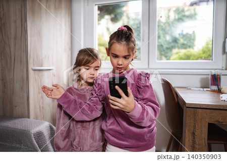 Little sisters looking at smartphone together in a kids room Little sisters looking at smartphone together in a kids room 140350903