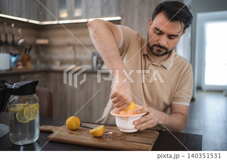 Man squeezing lemons in the kitchen preparing detox water or lemonade Man squeezing lemons in the kitchen preparing detox water or lemonade 140351531