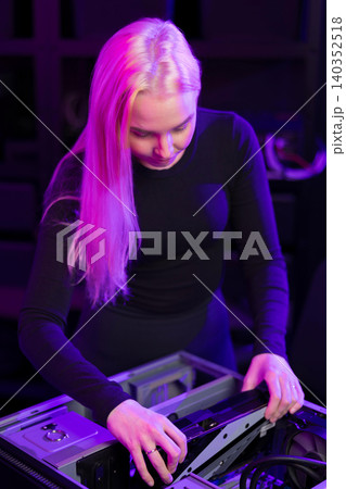 Young woman upgrading a gaming PC under purple lighting, assembling hardware components with focus 140352518
