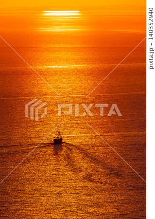 Small ship crossing golden sea at sunset with long reflection and orange sun light Small ship crossing golden sea at sunset with long reflection and orange sun light 140352940