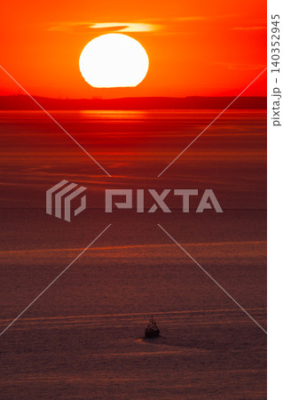 Ship sailing across glowing ocean during vibrant sunset from aerial perspective 140352945