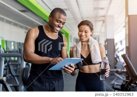 Trainer and client reviewing workout progress on clipboard after exercise at gym Trainer and client reviewing workout progress on clipboard after exercise at gym 140352963