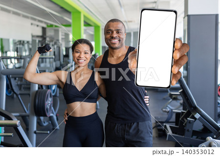 Young black standing in fitness center, presenting smartphone with blank screen Young black standing in fitness center, presenting smartphone with blank screen 140353012