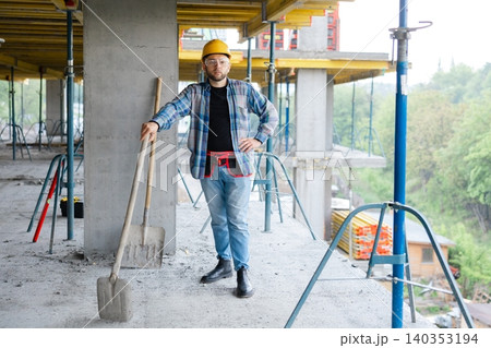 Construction worker standing with shovel at building site Construction worker standing with shovel at building site 140353194