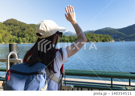 Woman waving on a pier at Lake Wolfgangsee in the Austrian Alps, illustrating summer lakeside travel and a nature tourism scene Woman waving on a pier at Lake Wolfgangsee in the Austrian Alps, illustrating summer lakeside travel and a nature tourism scene 140354511