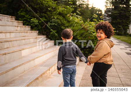 Diverse children friends holding hands walking through park stairs 140355043
