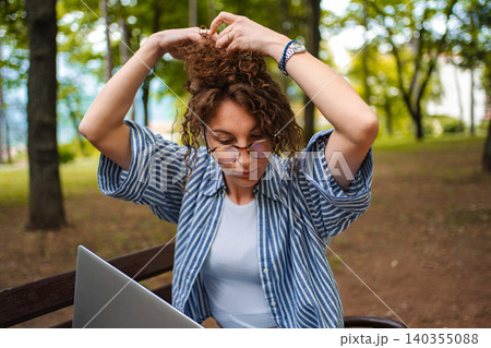 Woman working remotely with laptop in park styling hair 140355088