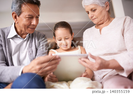 Family, grandparents and girl with tablet for entertainment, social media or research on sofa at home. Grandma, grandpa and child with smile on technology for online search, show or movie at house Family, grandparents and girl with tablet for entertainment, social media or research on sofa at home. Grandma, grandpa and child with smile on technology for online search, show or movie at house 140355159