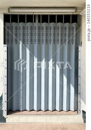 Accordion security gate with decorative cutouts and sunlight casting shadows 140355219