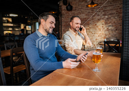 Men using smartphones in bar while drinking beer Men using smartphones in bar while drinking beer 140355226