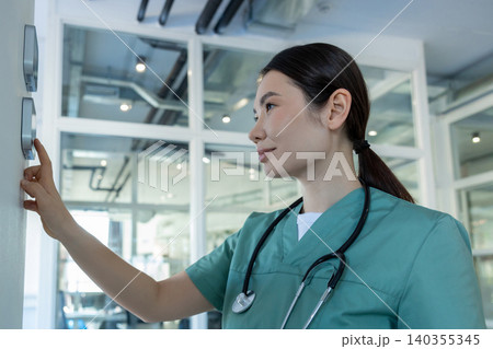 Dark-haired female doctor in lab coat setting the temperature range in a room Dark-haired female doctor in lab coat setting the temperature range in a room 140355345