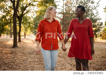 Two happy multi-ethnic women holding hands and walking in a park Two happy multi-ethnic women holding hands and walking in a park 140355465